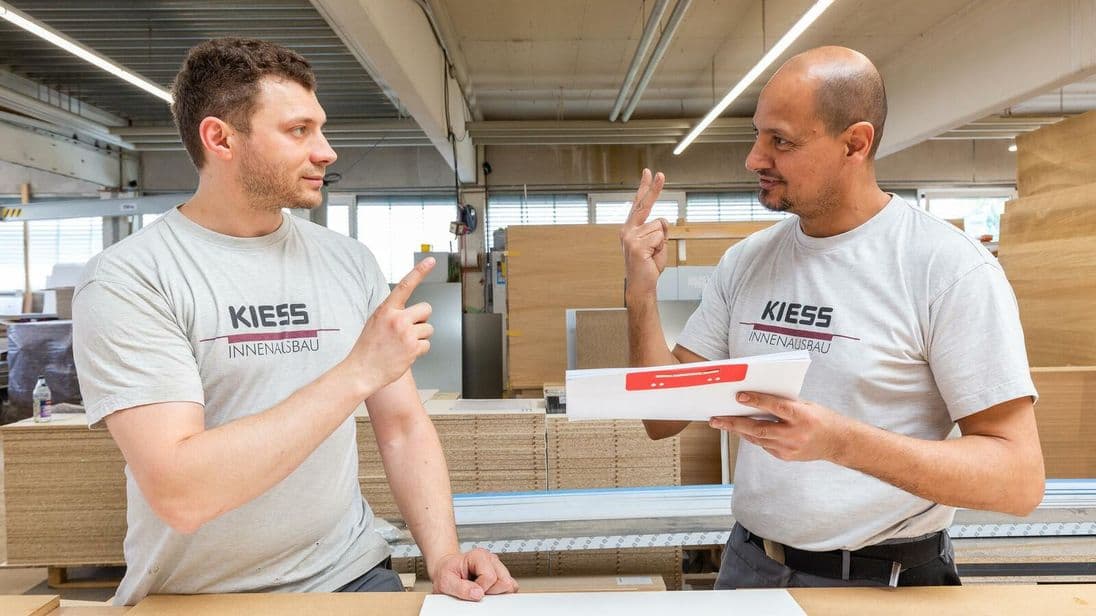 Hier versteht man sich auch ohne Worte: Gebärdensprache ergänzt die Kommunikation in der Werkstatt – eine Technik, die gehörlose Mitarbeiter in die Schreinerei gebracht haben.