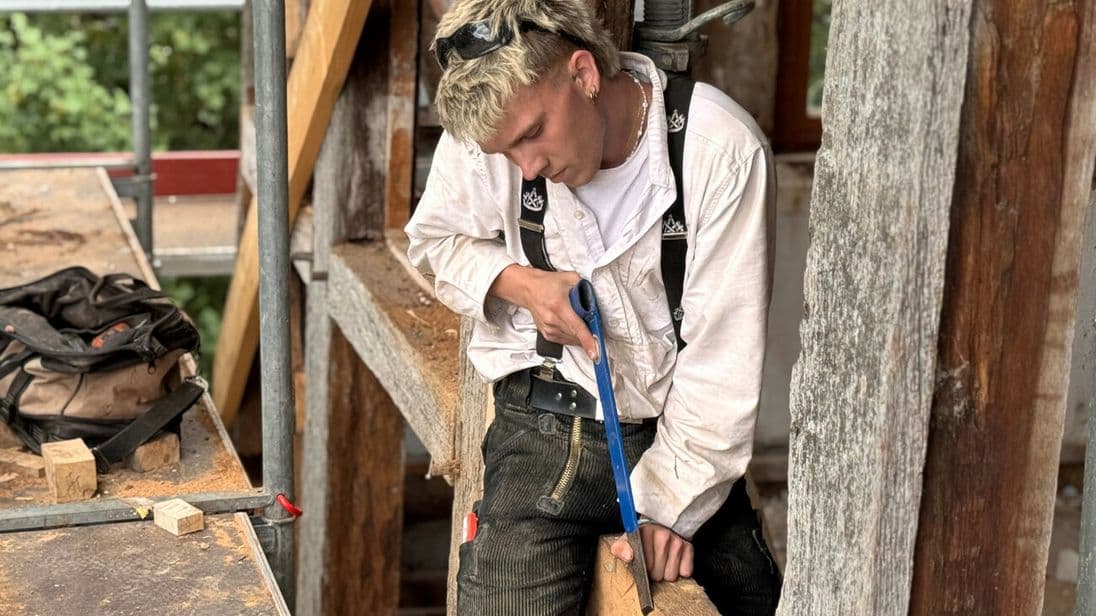 Auch der Auszubildende Leonhard packt kräftig mit an: Auf einem Balken sitzend macht er mit der Stoßaxt die Feinarbeit.