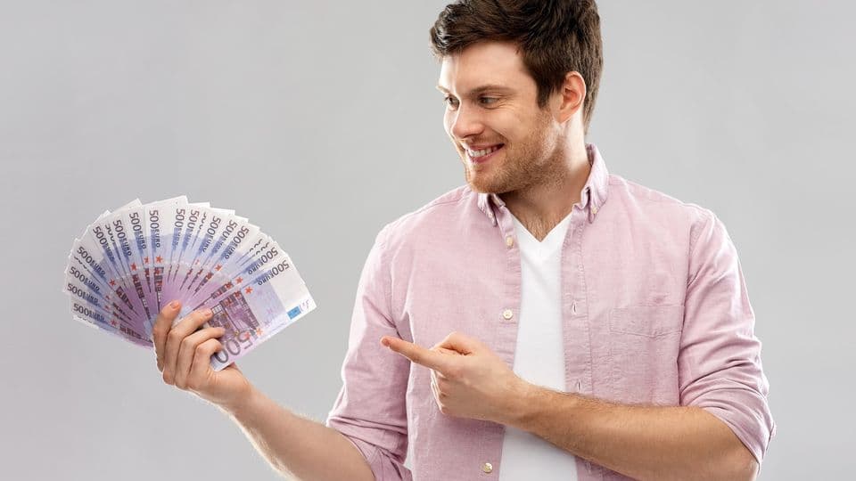 money, finance, business and people concept - smiling young man showing fan of five hundred euro bank notes over grey background