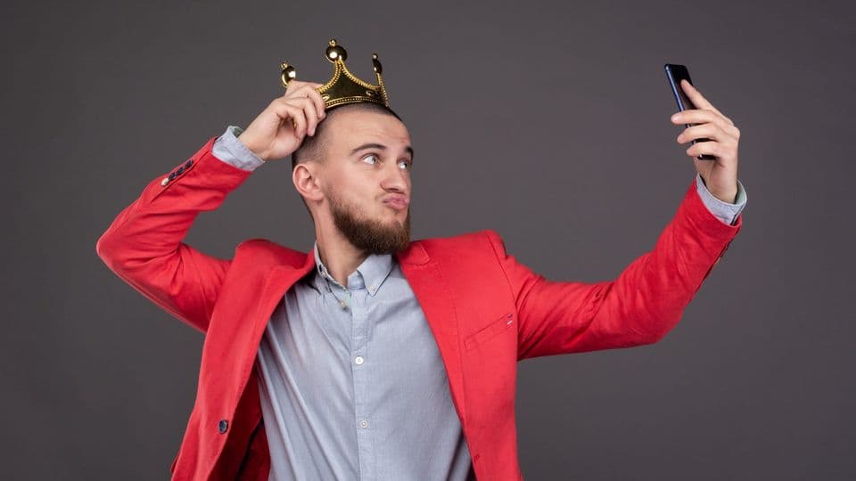 Mann mit goldener Krone auf dem Kopf macht ein Selfie.