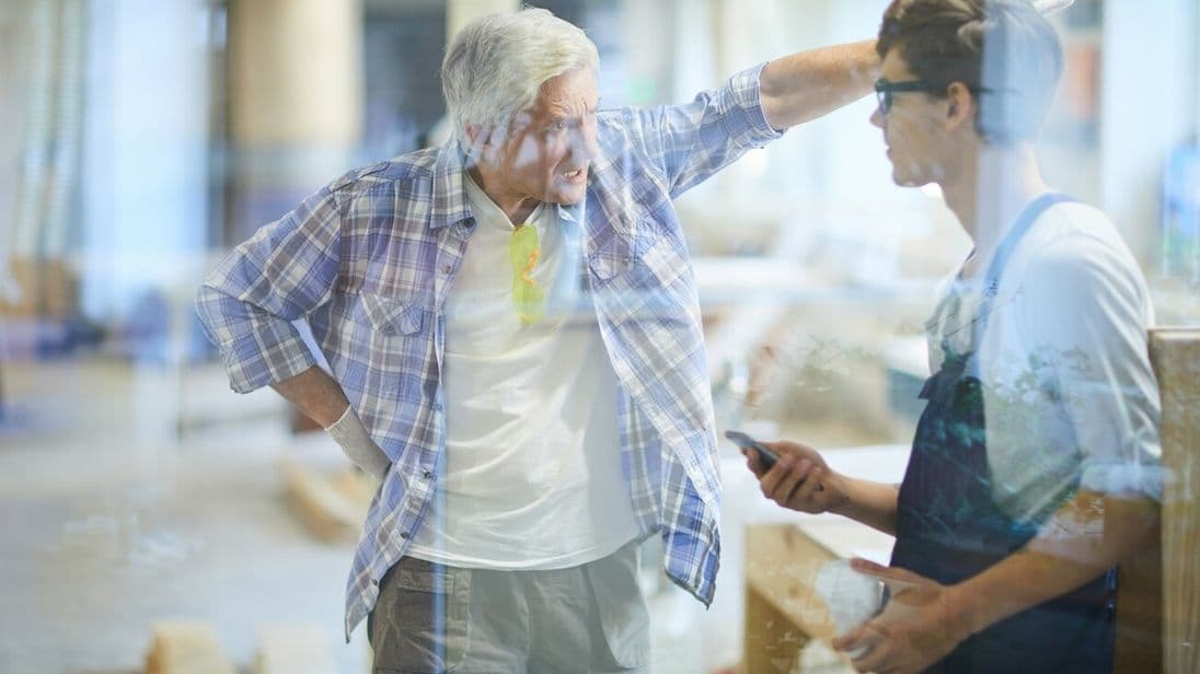 Furious emotional gray-haired mature carpenter foreman pointing with hand and yelling at lazy worker while dressing down him for poor performance in workshop