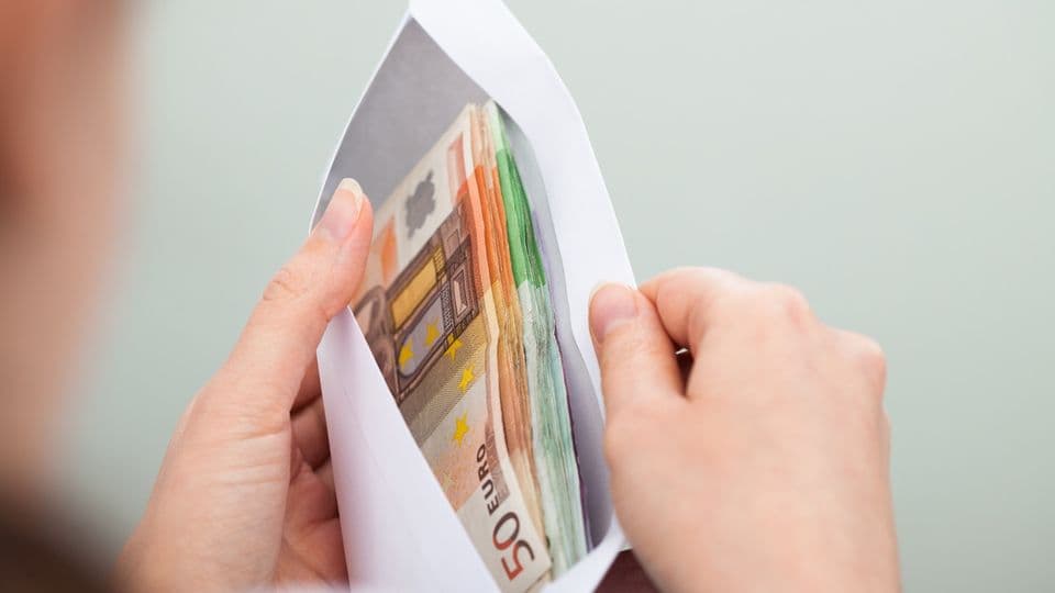 Eine Frau schaut in einen Briefumschlag, in dem diverse Euro-Noten enthalten sind.