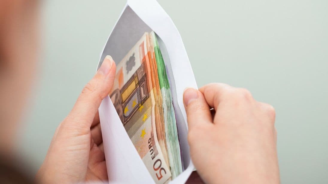Eine Frau schaut in einen Briefumschlag, in dem diverse Euro-Noten enthalten sind.