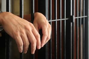 prisoner behind bars.hand of prisoner on steel jail bars.Man under arrested by policeman because illegal behaviour.